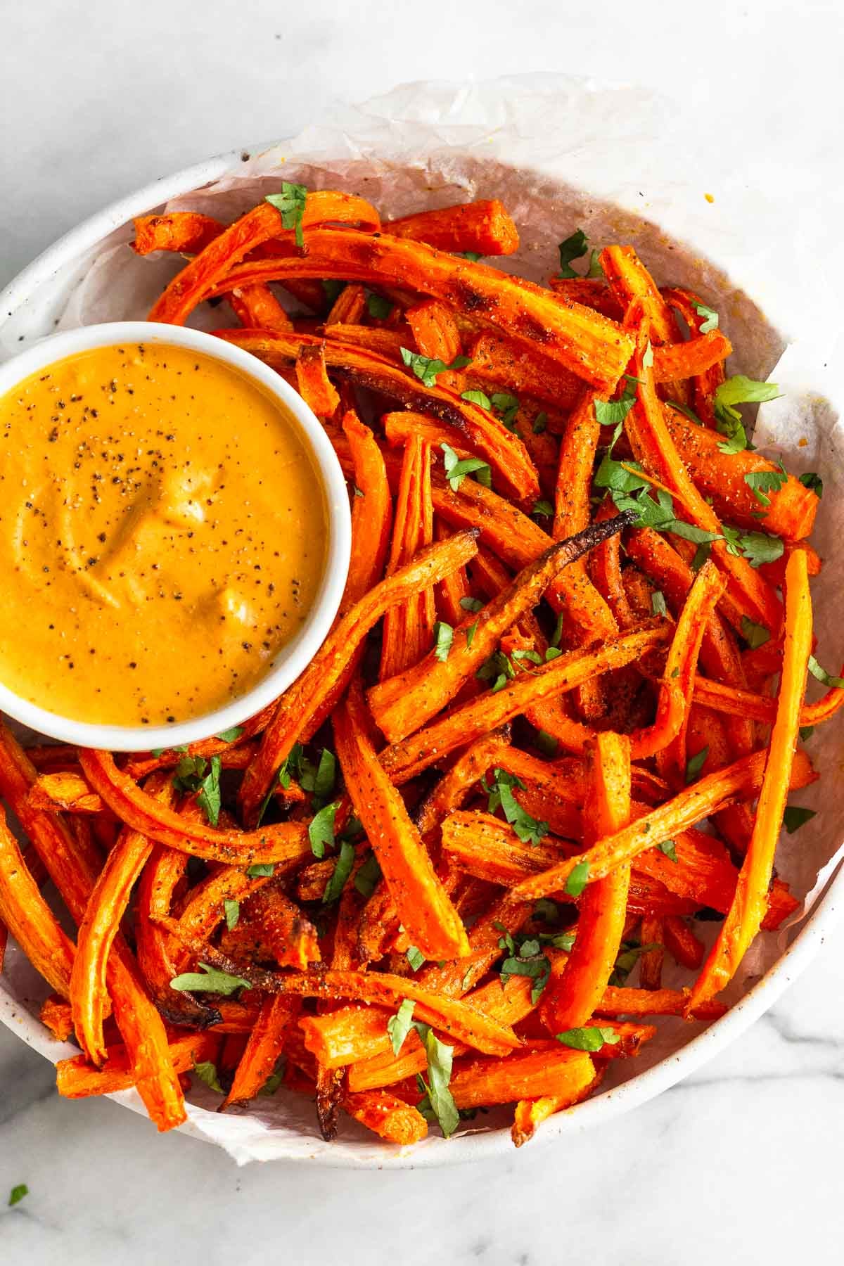 Overhead shot of carrot fries in a bowl topped with cilantro. In the bowl is a small ramekin with curry dipping sauce.
