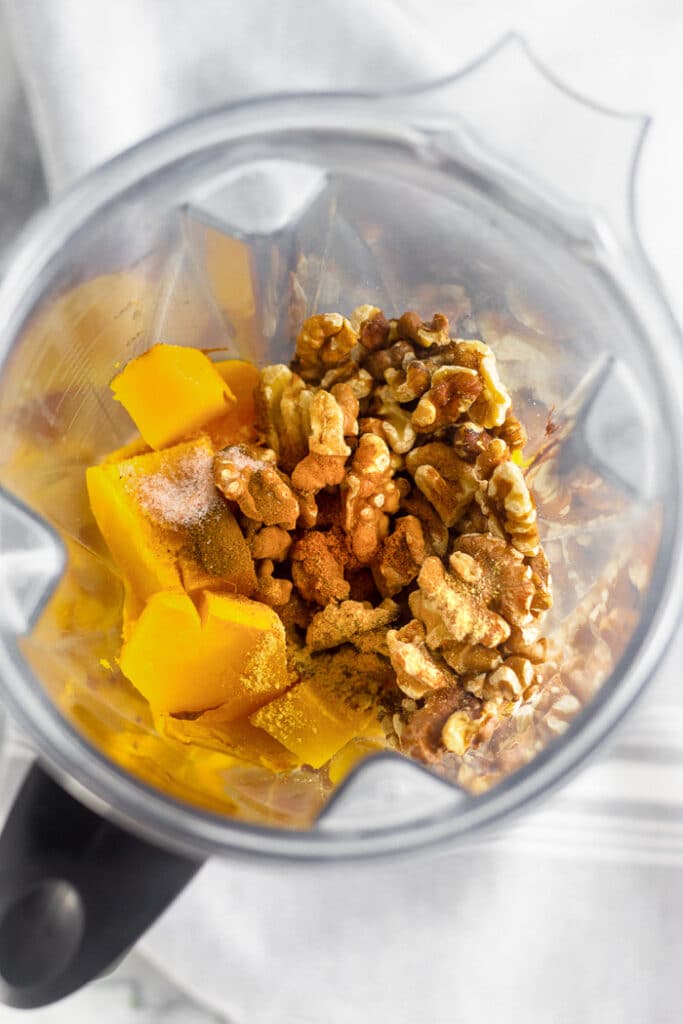 Overhead shot of a blender filled with roasted pumpkin, walnuts, and spice.