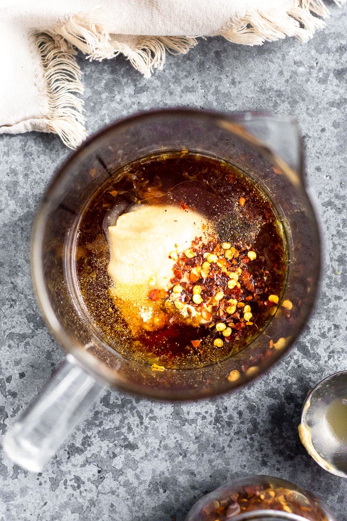 Glass mixing cup filled with coconut aminos, tahini, and spices to make vegan tahini dressing.
