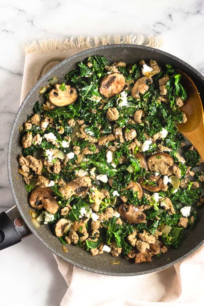 A large skillet filled with cooked ground turkey, kale, mushrooms, onion, and goat cheese going to used as the filling for spaghetti squash with ground turkey.