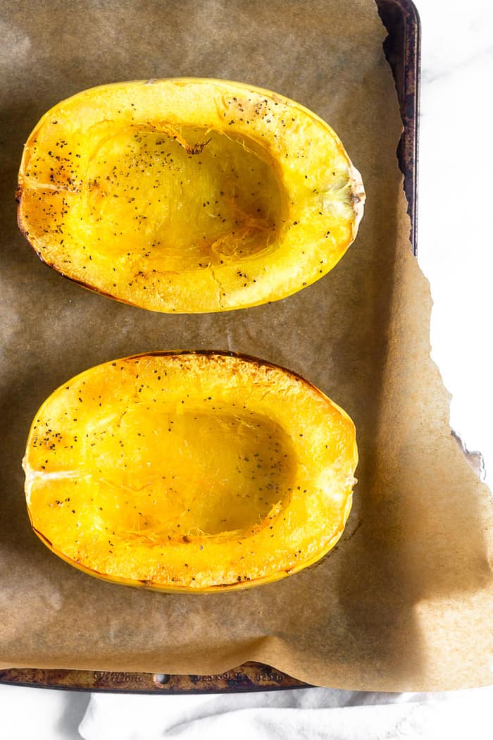 Two halves of spaghetti squash sitting on a baking sheet. They just came out of the oven.