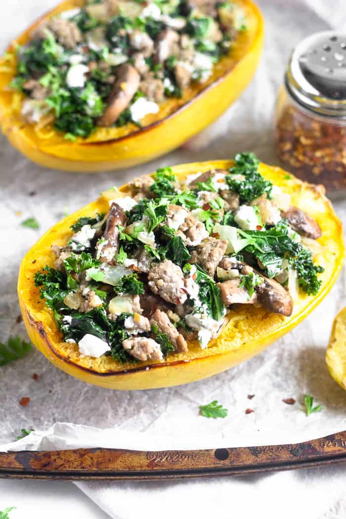 Two turkey kale spaghetti squash boats sprinkled with fresh parsley and red pepper flakes on a baking sheet.