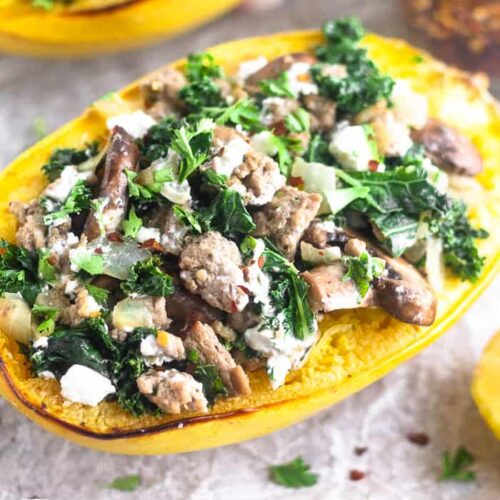 A turkey kale spaghetti squash boat sitting on a baking sheet. It is surrounded by half a lemon, a jar of red pepper flakes, and another spaghetti squash boat behind it.