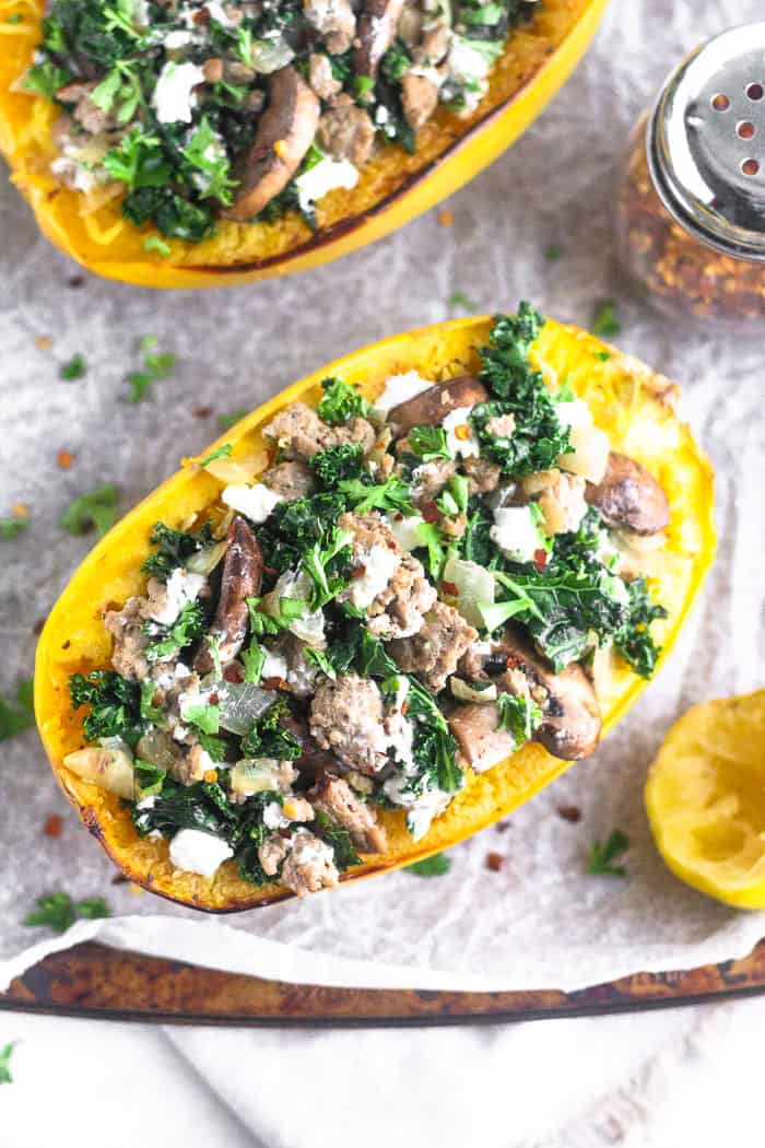 Overhead view of two turkey kale spaghetti squash boats on a baking sheet. They are surrounded by half a lemon and har of red pepper flakes.