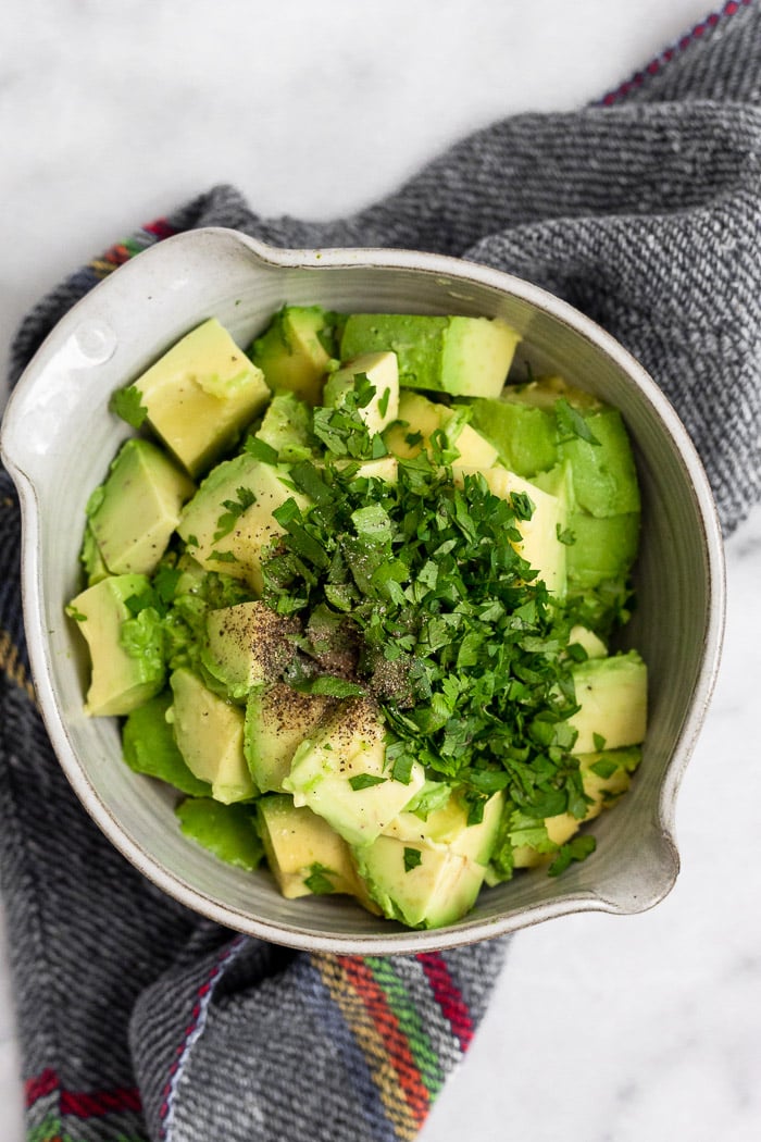 A small bowl filled with diced avocado, cilantro, and salt and pepper.