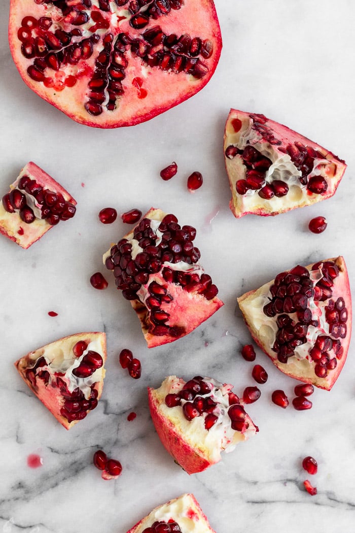 A pomegranate broken up into small pieces spread out on a white counter.