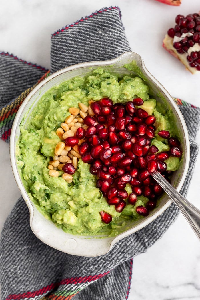 Small bowl filled with smashed avocado, toasted pine nuts, and pomegranate arils.