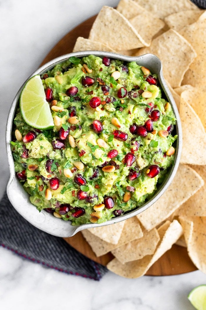 Large plate filled with chips and a bowl of pomegranate guacamole topped with a lime wedge.