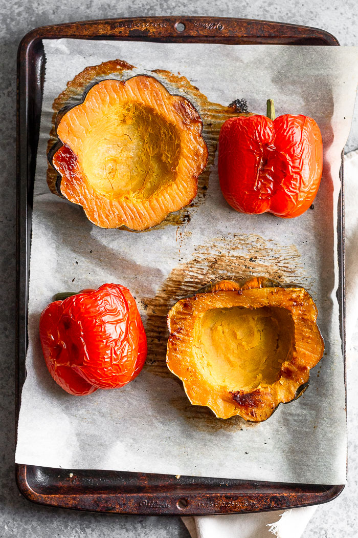 Baking sheet lined with parchment paper with 2 halves of roasted acorn squash and 2 roasted red peppers.