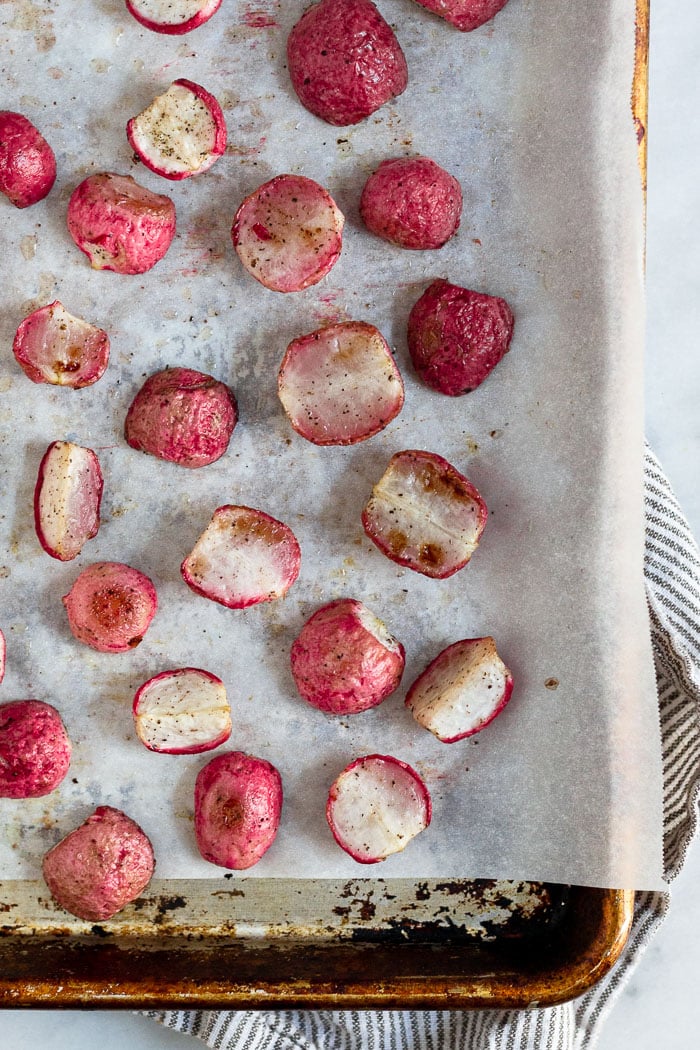 A baking sheet with parchment paper on it with halved radishes that were just roasted in the oven.