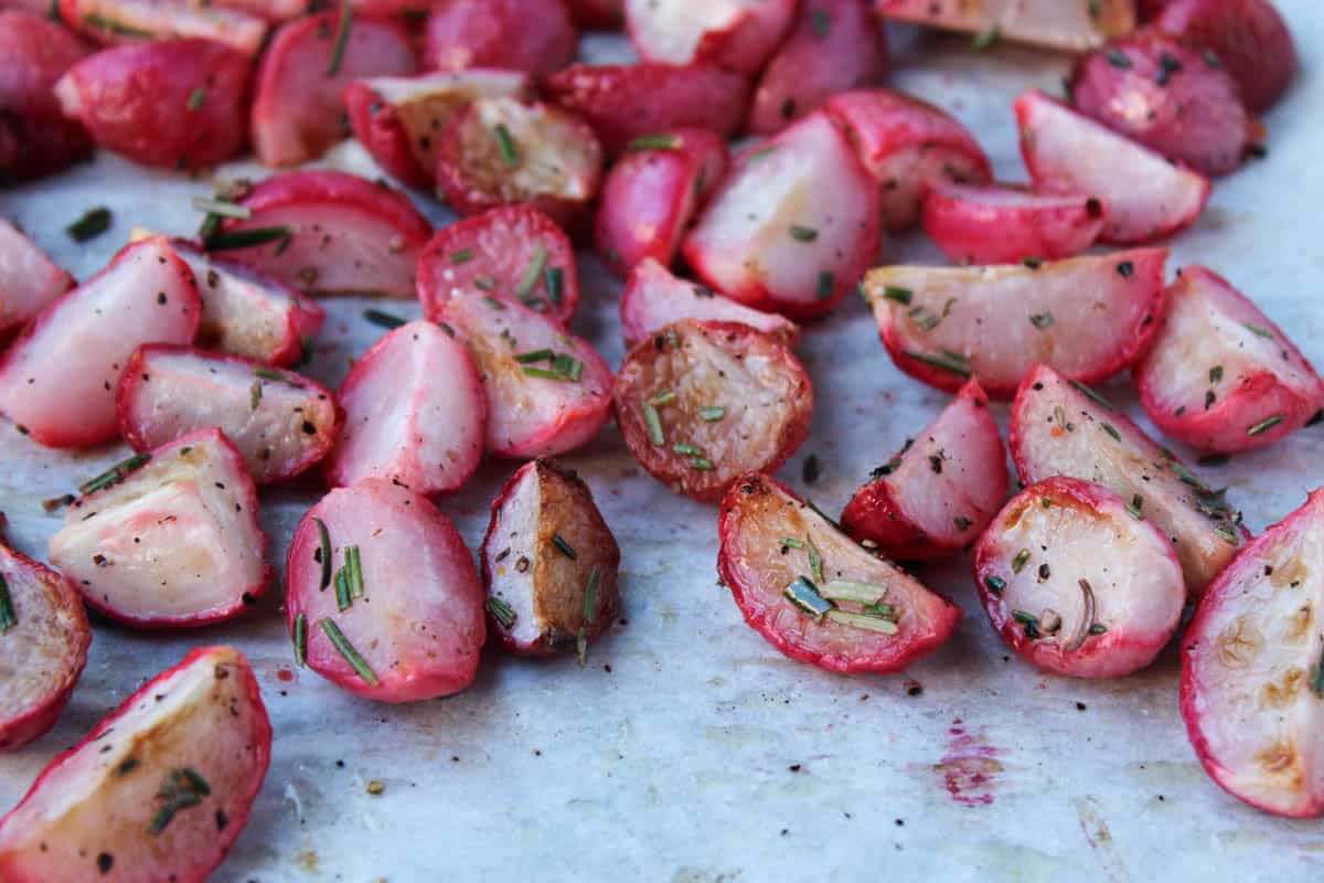 Rosemary roasted radishes on a baking sheet topped with fresh rosemary