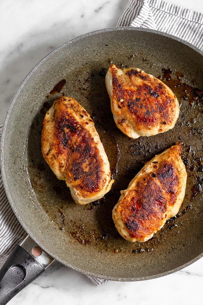 Large saute pan filled with 3 seasoned and cooked chicken breasts.