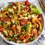 Vietnamese Chicken Cabbage Salad in a white bowl on a blue and white striped towel. Around it are chopsticks, a bowl of cashews, and lime wedges.