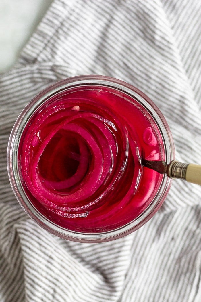 A jar of quick pickled onions with a fork coming out of them. They are sitting on a striped towel.