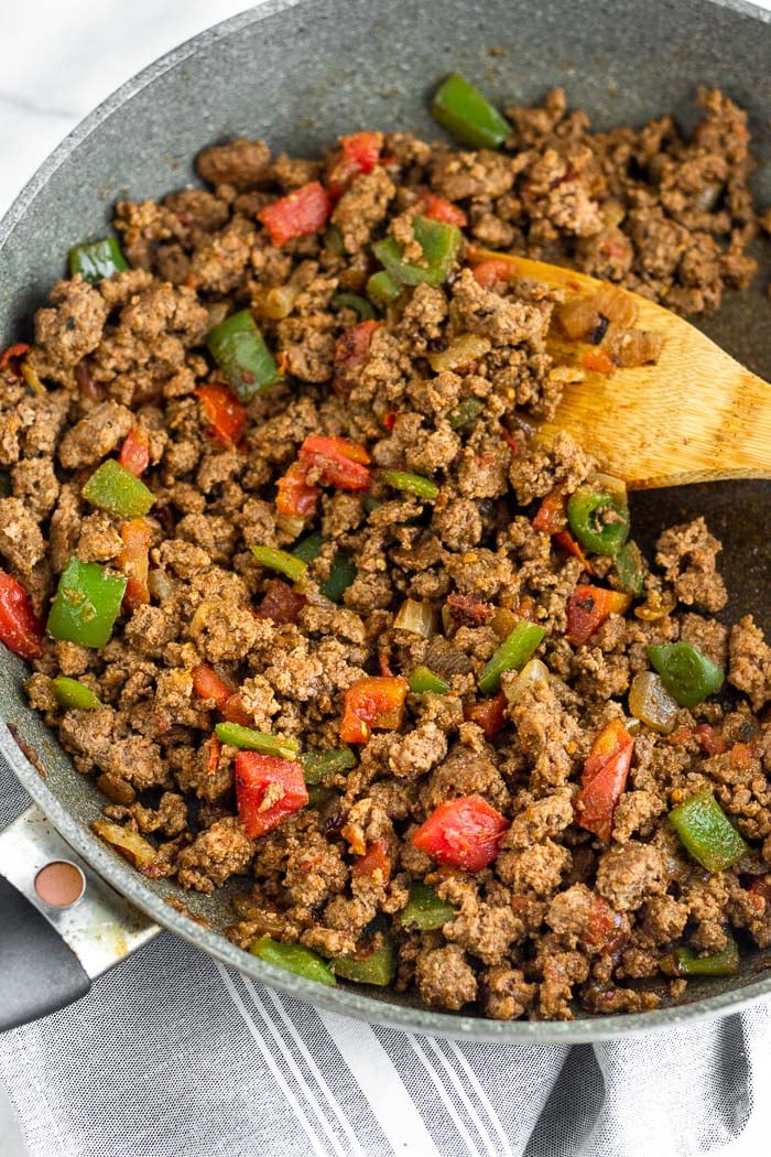 A large skillet filled with cooked taco meat with a wooden spoon coming out of it.