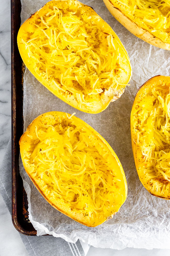A large baking sheet with halves of cooked spaghetti squash on it.