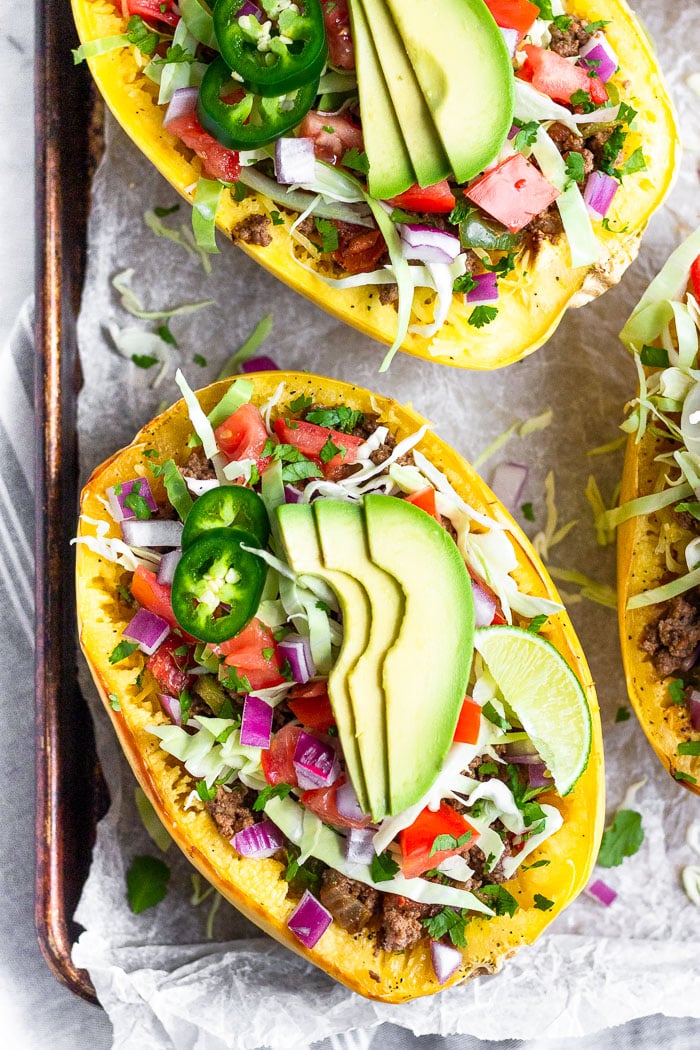 Overhead shot of 3 taco spaghetti squash boats topped with cabbage, tomatoes, onion, avocado, and jalapeños on a baking sheet .