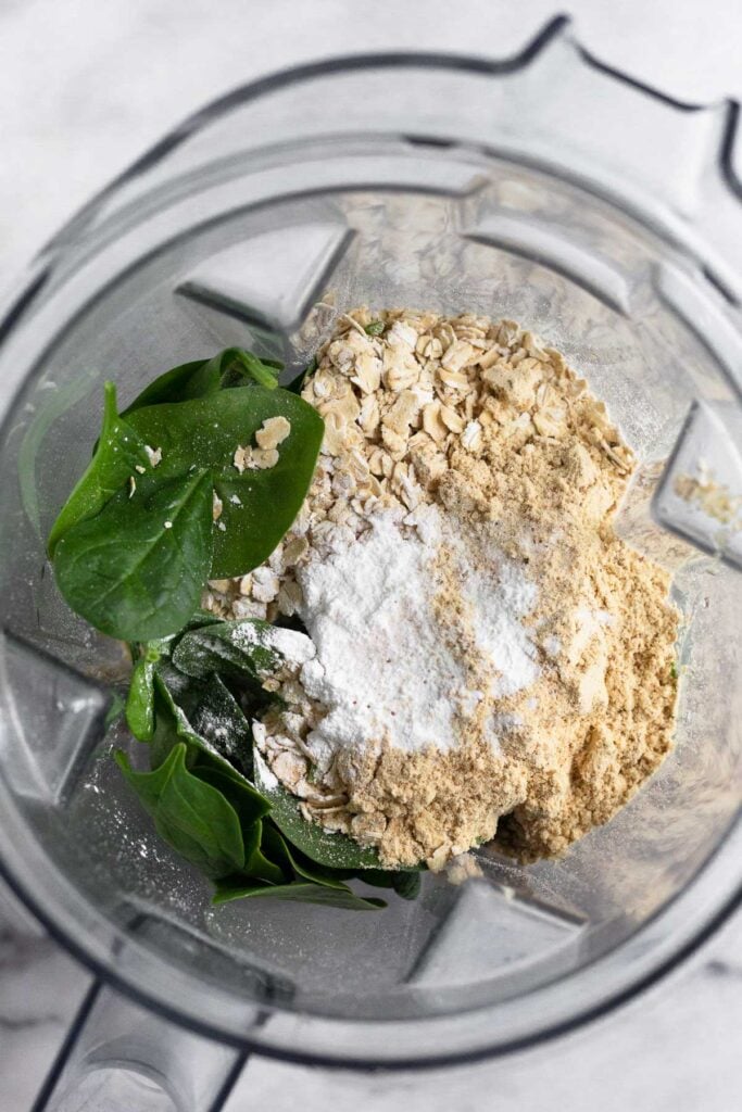 Blender filled with spinach, oats, protein powder, baking powder.