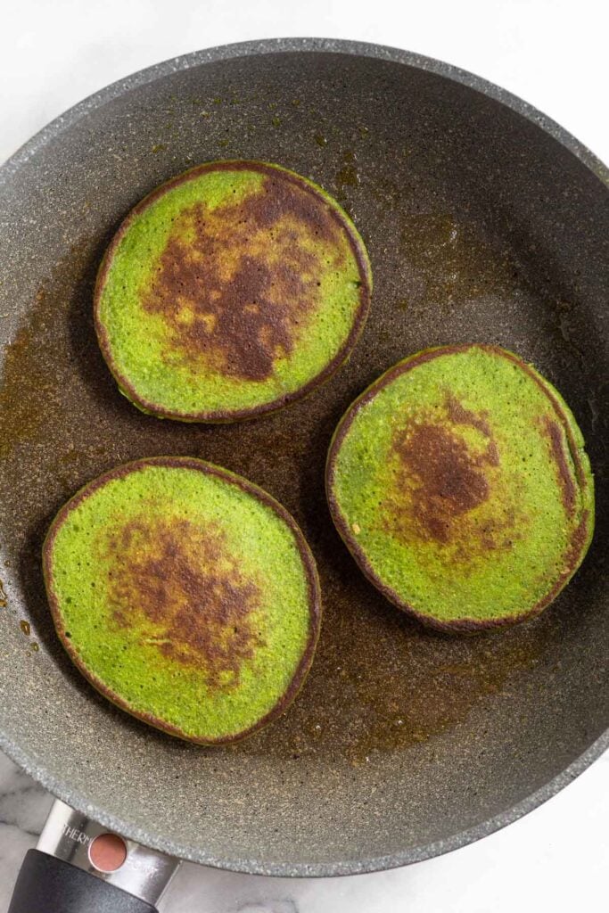 Three spinach pancakes in a large skillet.