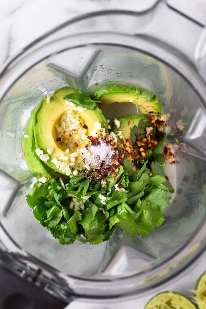 Blender filled with coconut milk, avocados, lime juice, cilantro, and spices.