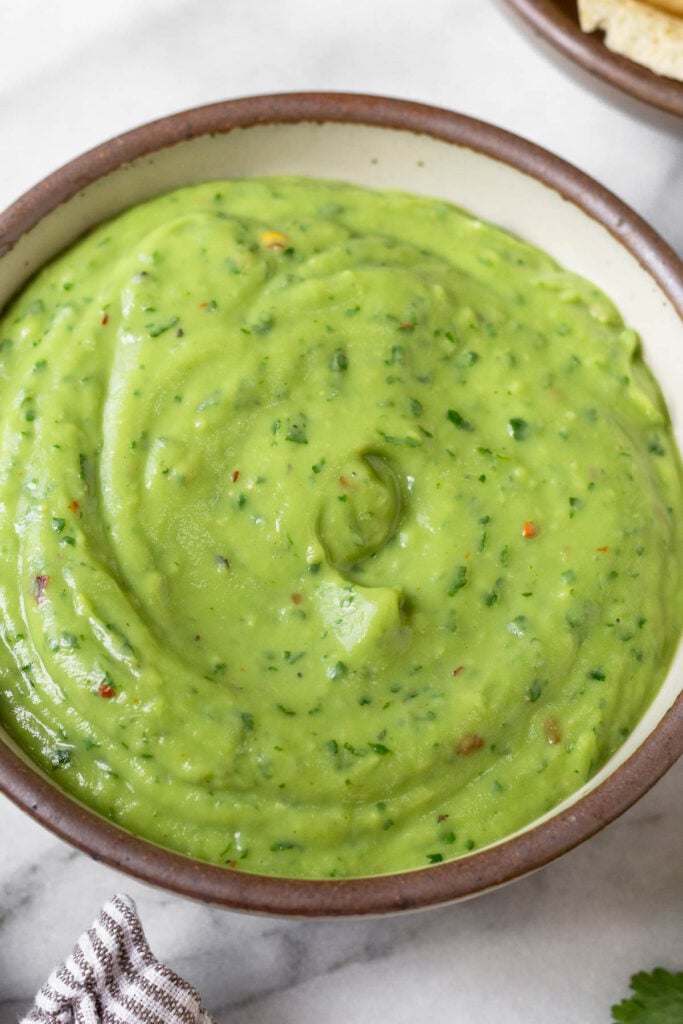 Close up of creamy avocado sauce in a white bowl.