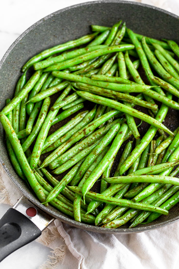 Large sauté pan filled with sesame garlic green beans sitting on a tan linen.