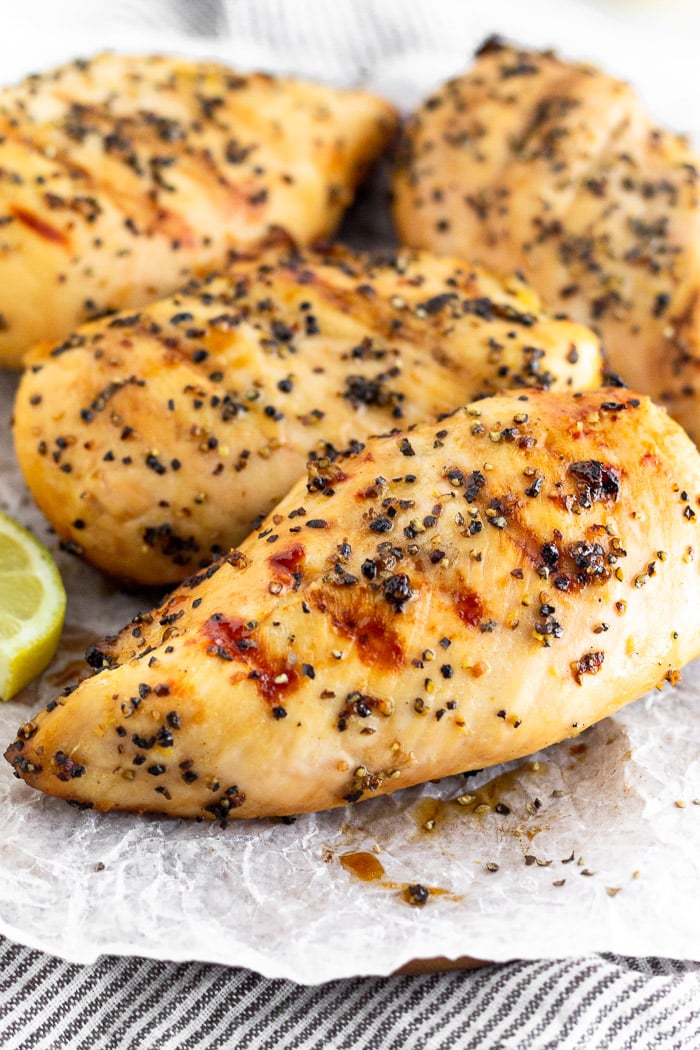 Close up of grilled lemon pepper chicken breasts on a plate garnished with some lemon slices.