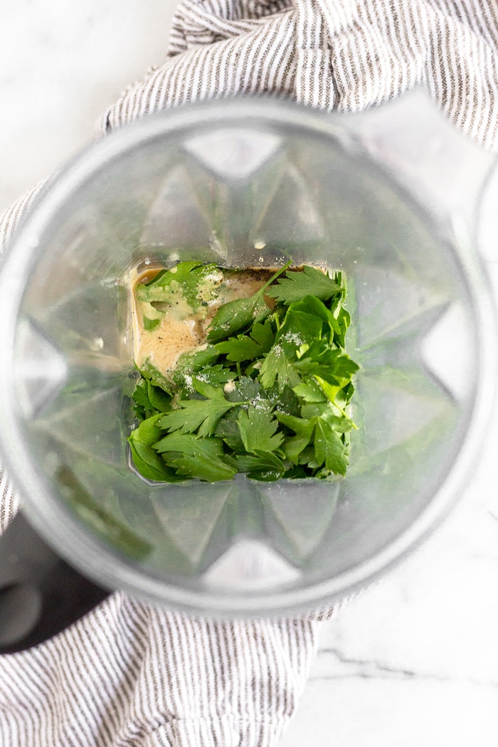 Blender filled with tahini, fresh parsley, lemon juice, salt, and water.