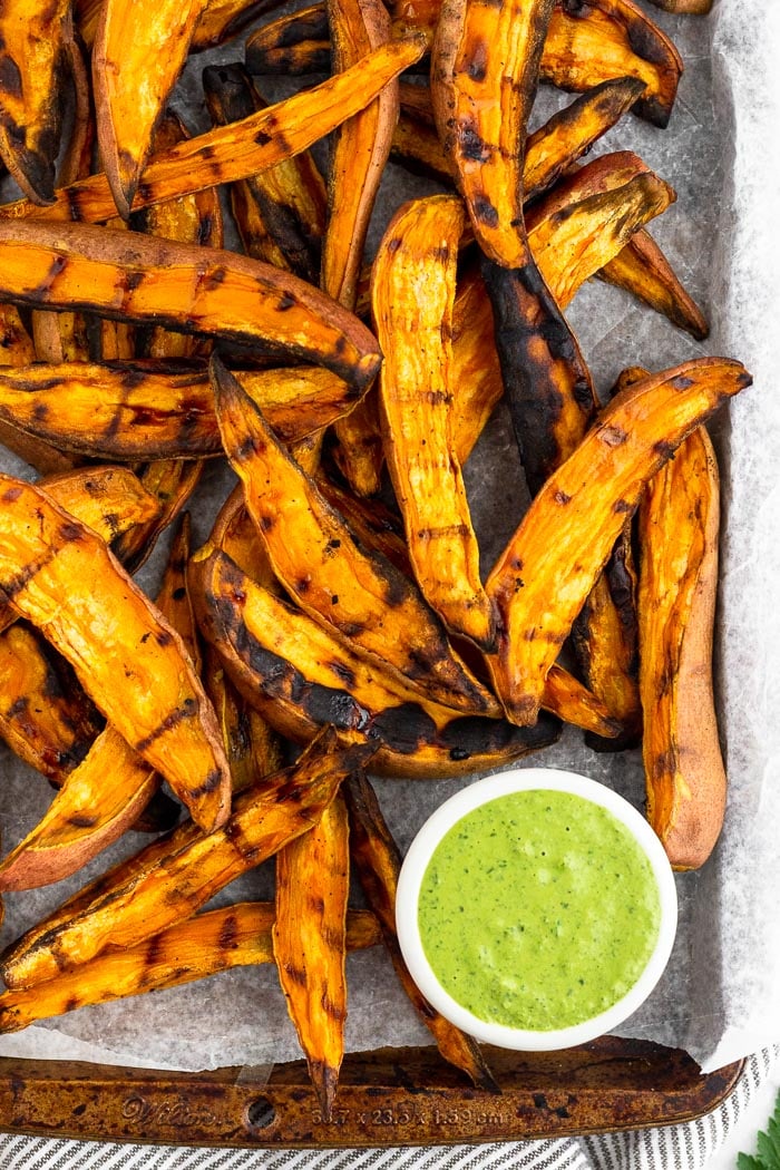 Baking sheet filled with grilled sweet potato fries and a bowl of green dipping sauce.