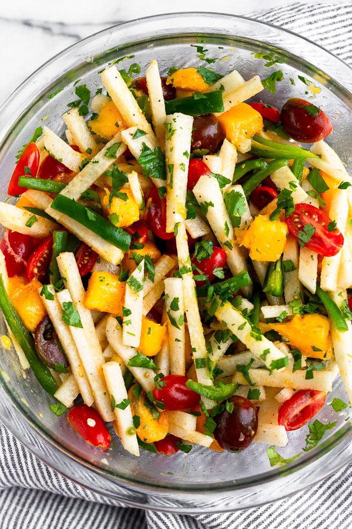 Large glass bowls filled with jicama salad with tomatoes, mango, jalapeños, and cilantro.