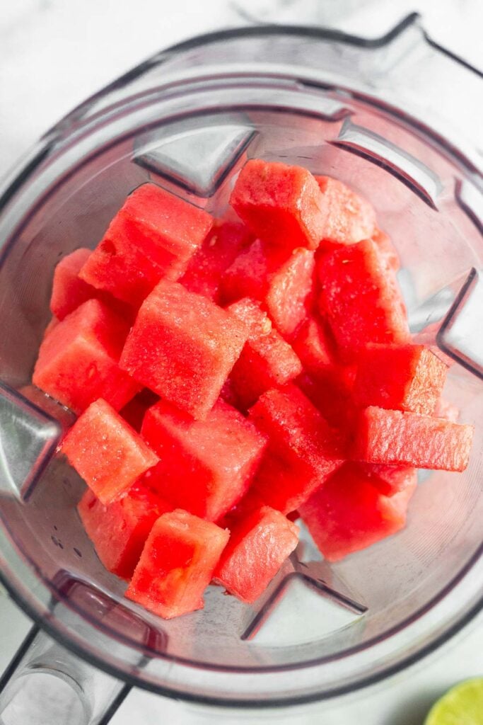 Blender filled with frozen watermelon with half a lime next to it.