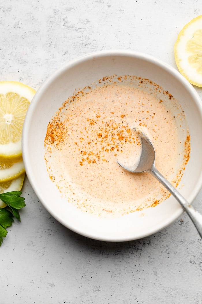 Bowl of Old Bay mayo with a spoon in it. Next to it is sliced lemons.