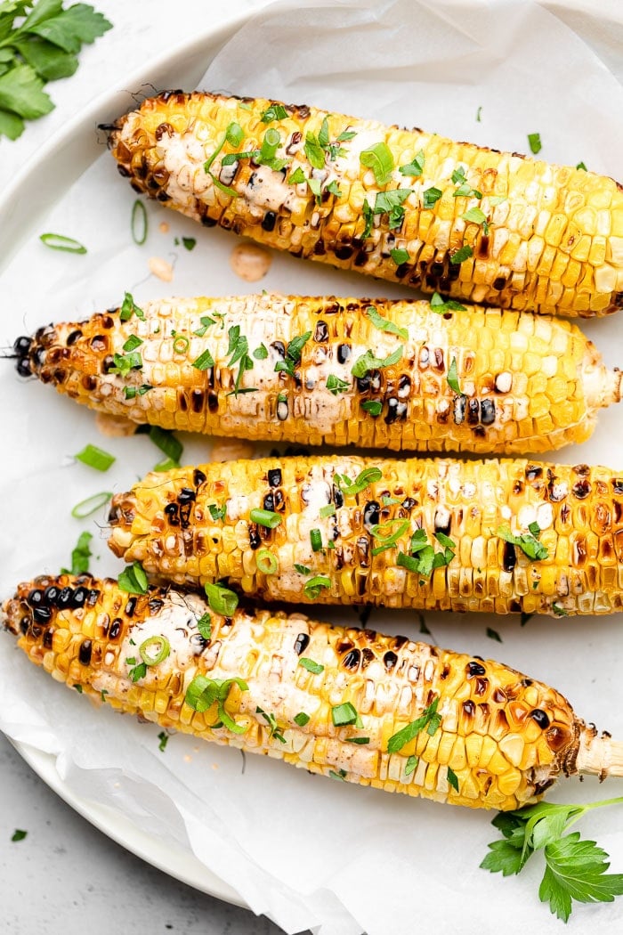 Grill corn on the cob on a large plate topped with mayo and herbs.