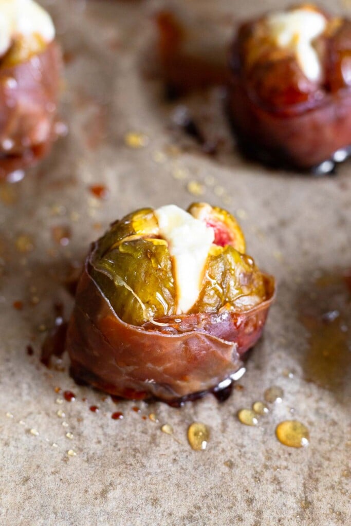 Baked figs wrapped in prosciutto stuffed with goat cheese and drizzled with honey on a baking sheet.