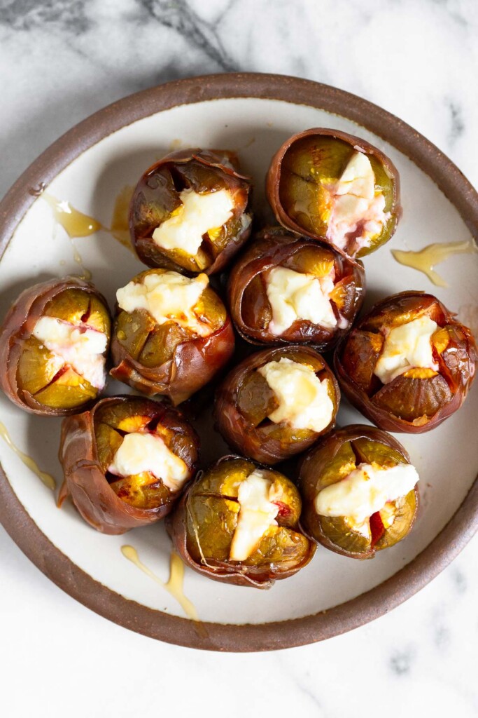 Overhead shot of baked figs stuffed with goat cheese and wrapped in prosciutto.