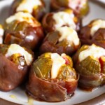 Prosciutto wrapped figs stuffed with goat cheese and drizzled with honey on a white plate.