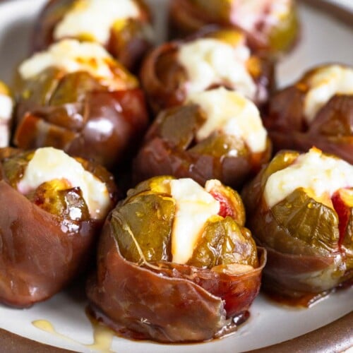 Prosciutto wrapped figs stuffed with goat cheese and drizzled with honey on a white plate.
