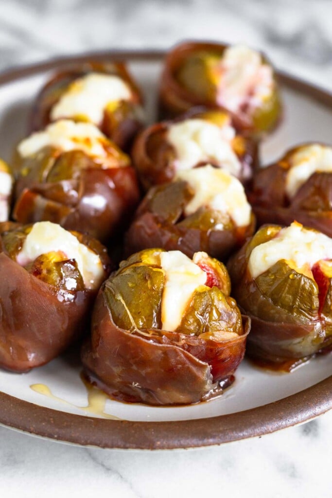 Prosciutto wrapped figs stuffed with goat cheese and drizzled with honey on a white plate.