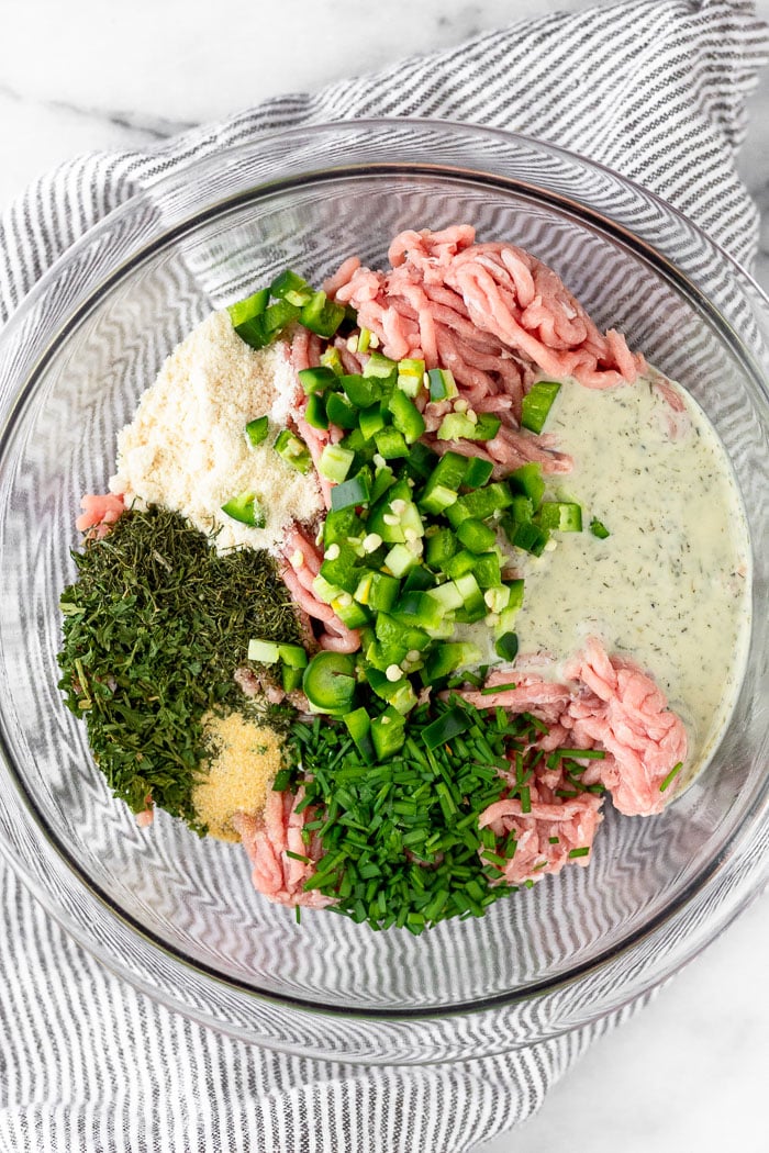 Bowl of raw ground turkey, spices, ranch dressing, coconut flour, and chopped jalapeños.
