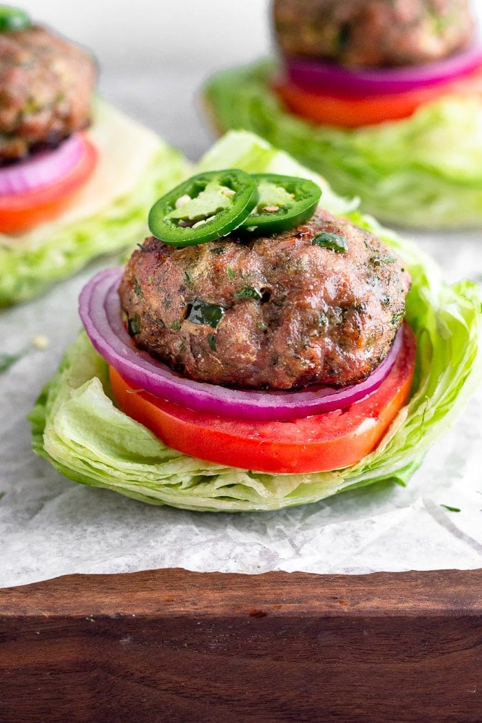 Ranch turkey burger topped with sliced jalapeños sitting on a lettuce cup with tomato and red onion. More burgers are behind it.