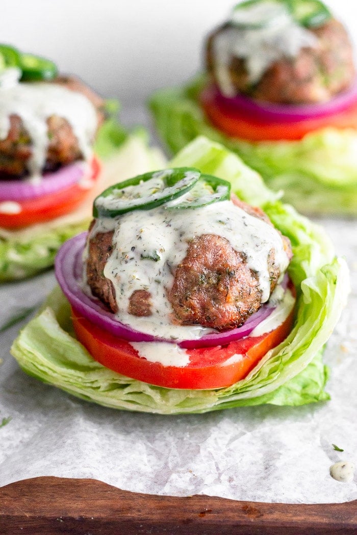 Paleo turkey burgers topped with fresh jalapeños and ranch dressing . They are in lettuce buns with tomato and red onion.