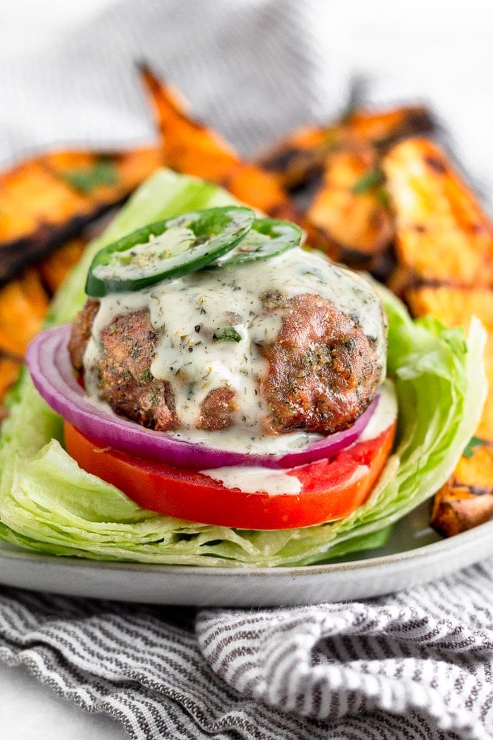Ranch turkey covered with ranch dressing and fresh jalapeños on a lettuce bun with tomato and onion. It is sitting on a plate with sweet potato fries.