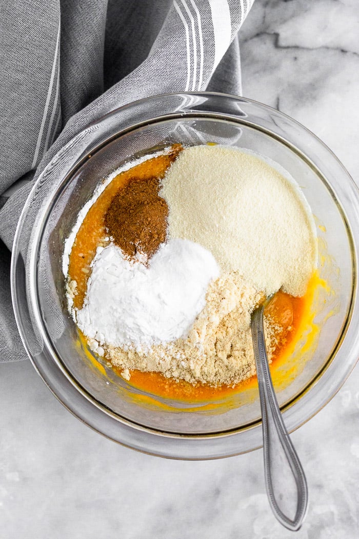 Glass bowl with pumpkin puree, eggs, flour, spices, baking soda, and protein powder in it. A fork is sticking out of it.