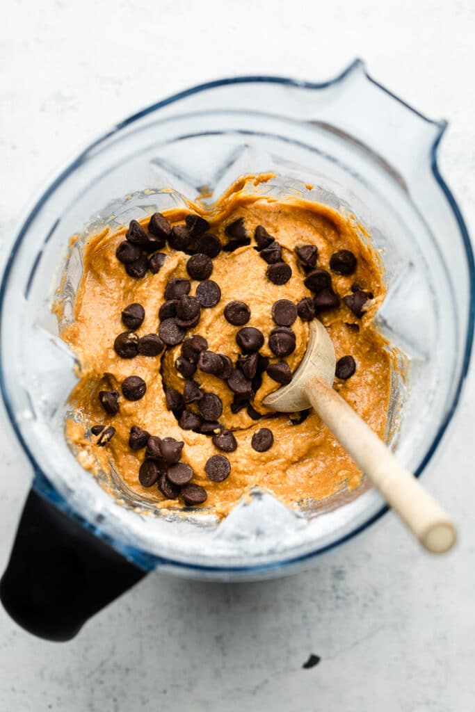 Blender filled with protein muffin batter sprinkled with chocolate chips. A wooden spoon is in the batter.
