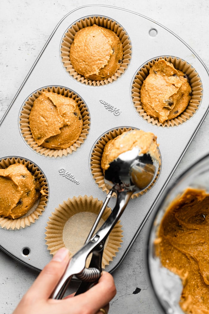 Protein muffin batter being scooped into a muffin tin lined with muffin cups.