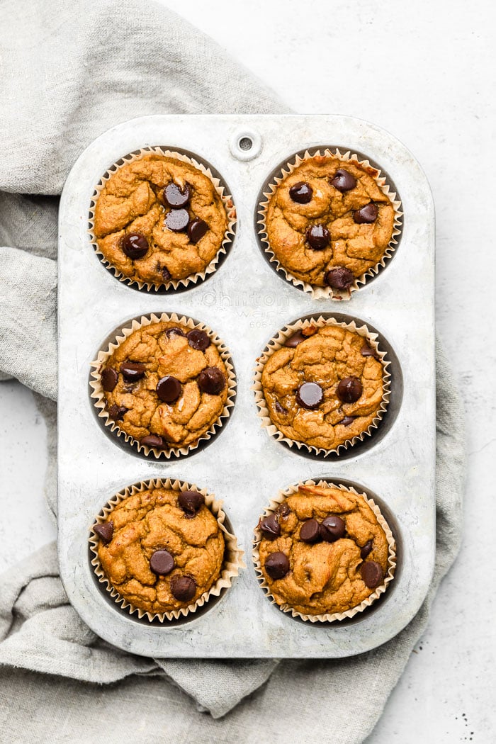 Overhead shot of 6 pumpkin protein muffins in a muffin pan on a tan linen.