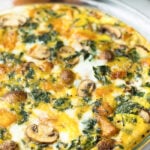 Crustless pumpkin quiche in a pie pan with eggs, pumpkin, and kale behind it.