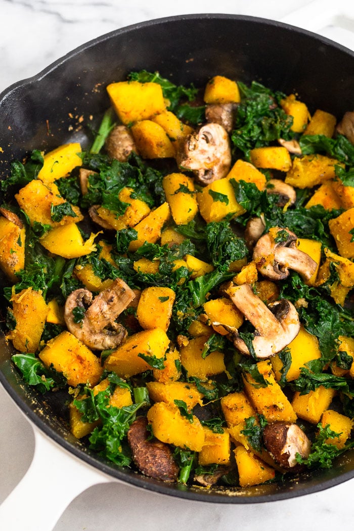 Pan filled with cooked diced pumpkin, kale, mushrooms, and spices.