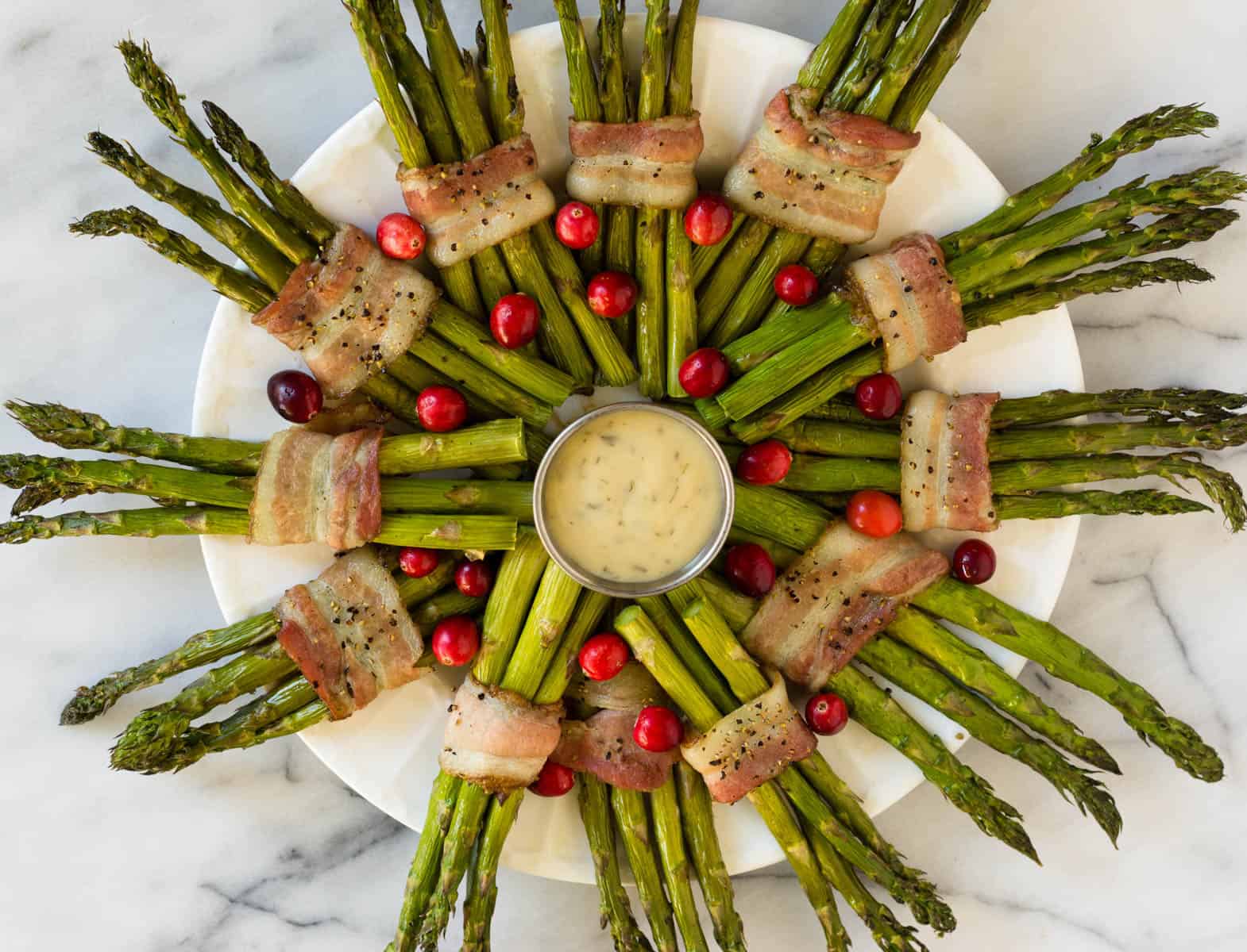 Fun and festive paleo & Whole30 dish with only a few ingredients, a Bacon Wrapped Asparagus Wreath make the perfect appetizer or side at holiday gatherings! - Eat the Gains