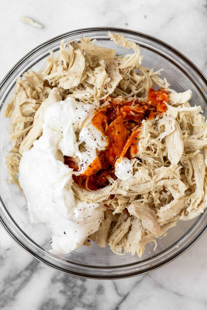 Bowl of shredded chicken with greek yogurt and hot sauce on top of it.
